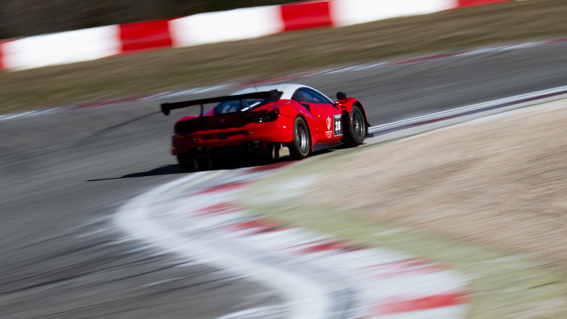 Ferrari 488 GT3 Evo in rot mit weißem Dach, der durch eine Schikane auf einer Rennstrecke fährt.