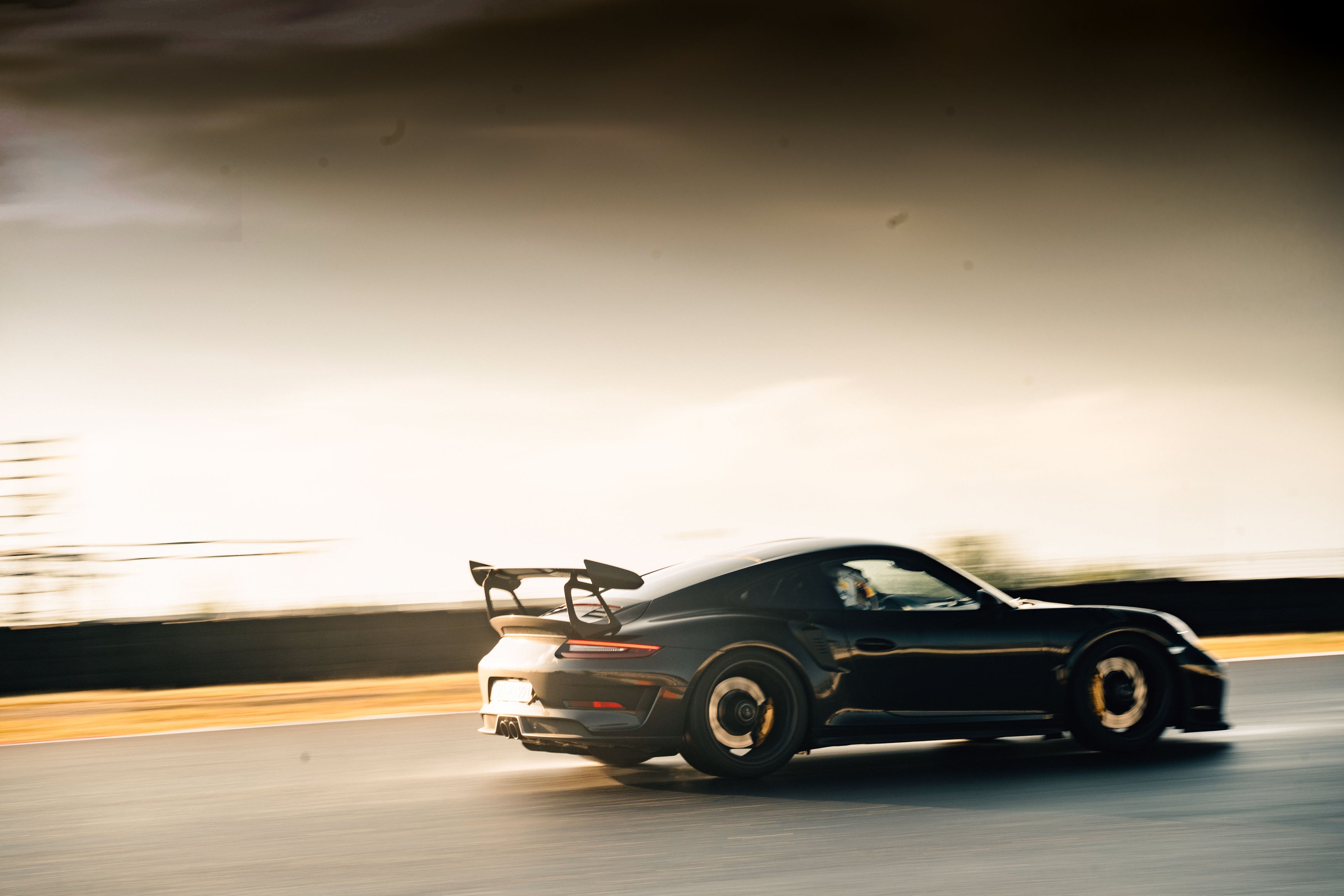 Schwarzer Porsche 991.2 GT3 RS mit schwarzen Felgen auf einer Rennstrecke bei Abendstimmung.