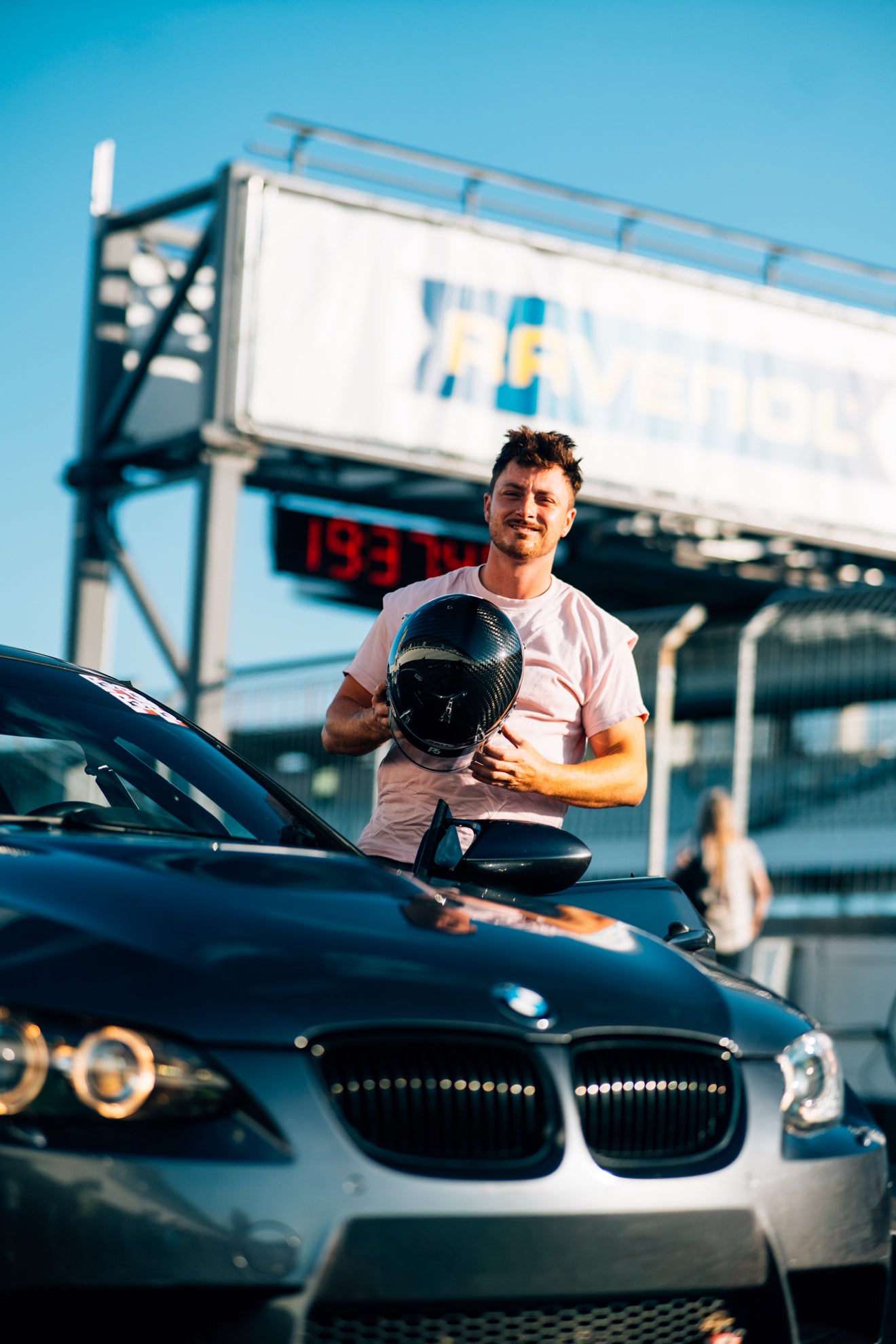 Timo Schahl neben seinem BMW e92 M3 Tracktool in Spacegrey mit einem Carbon Rennhelm auf dem Hockenheimring.