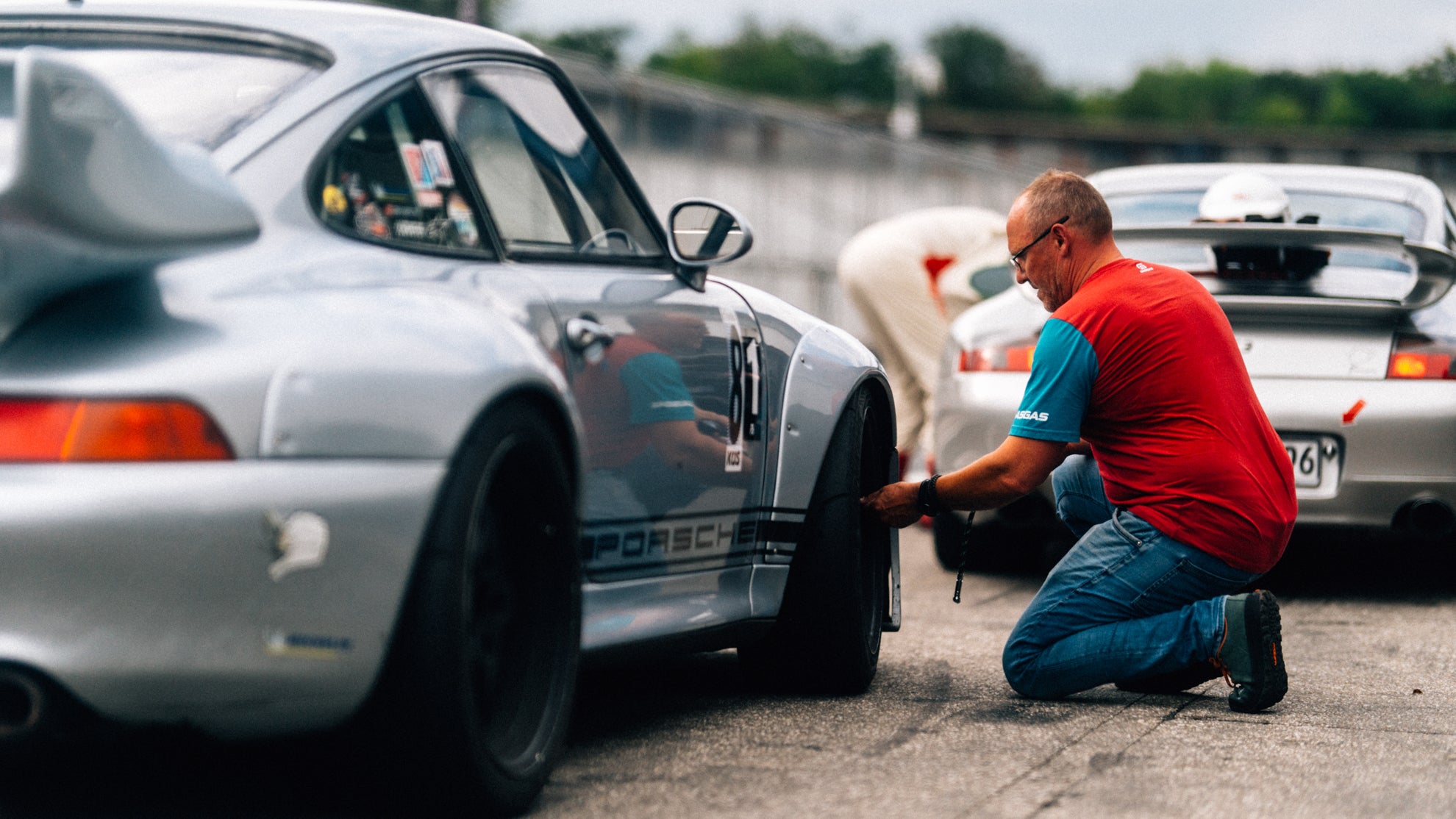 Silberner Porsche 993 RSR mit einem Fahrer , der den Luftdruck seines Sportwagen in der Boxengasse prüft.