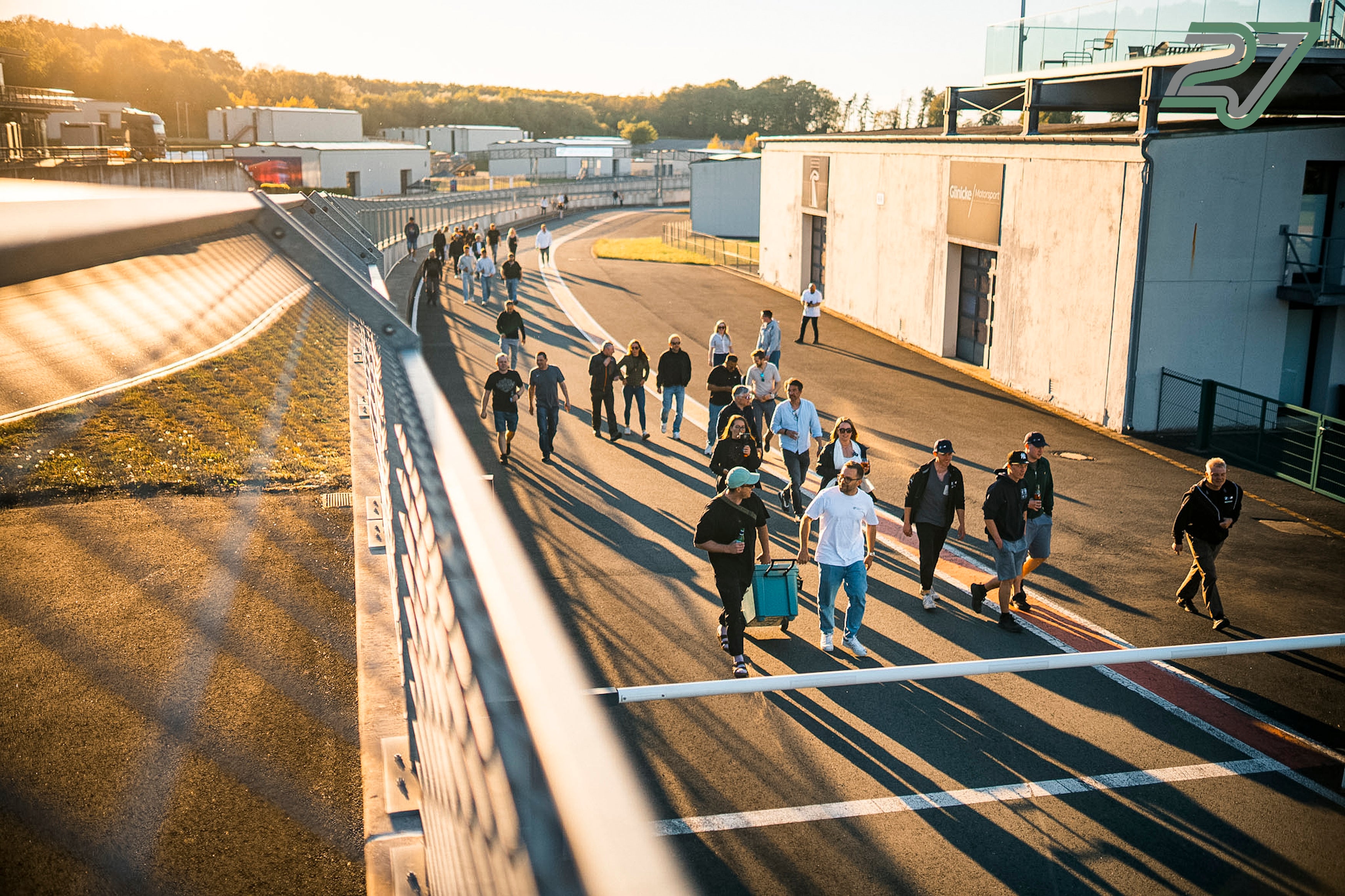 Teilnehmer eines TWENTYSEVEN Trackdays gehen im goldenen Abendlicht über die Rennstrecke am Bilster Berg